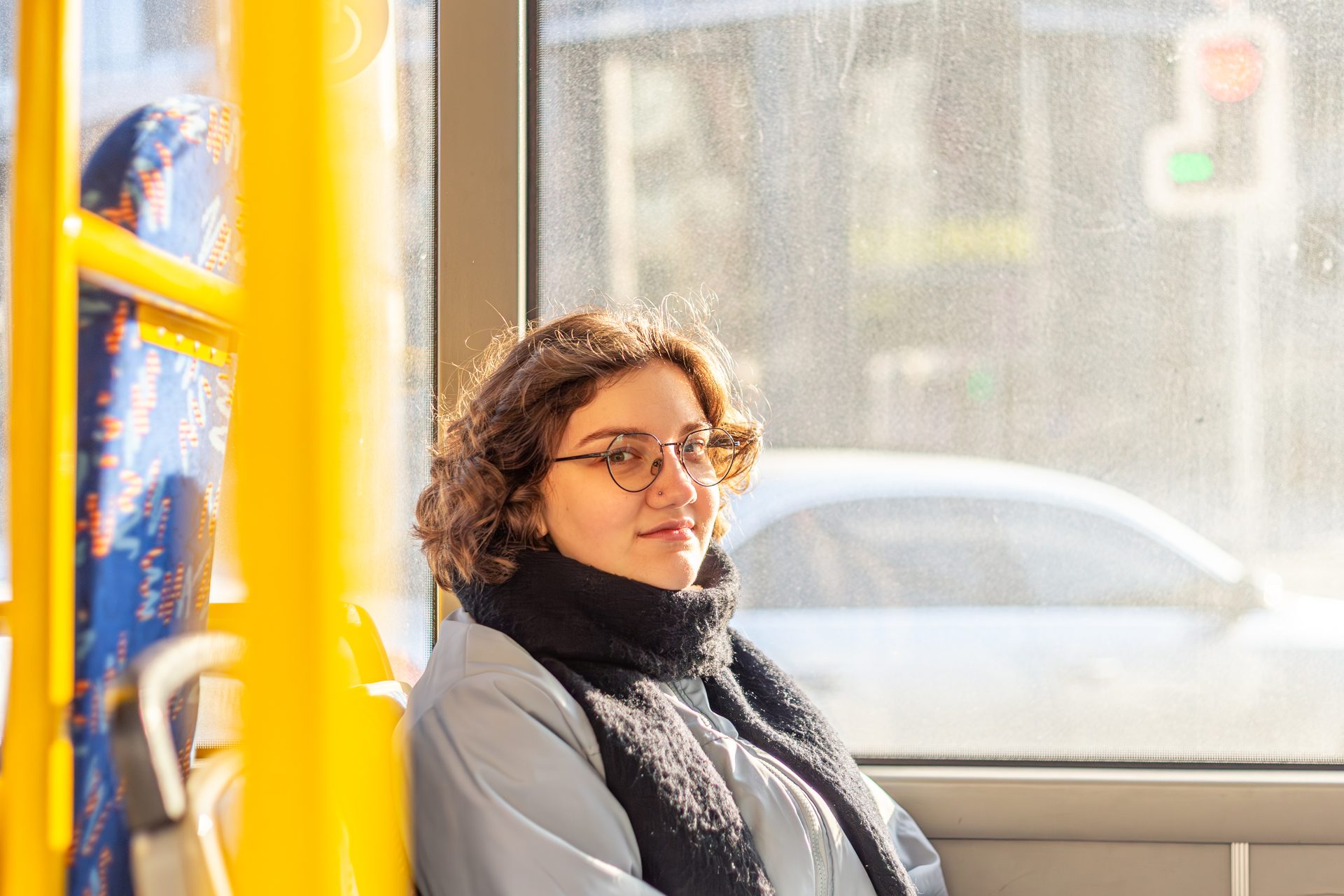 Studentka w okularach i szaliku jedzie miejskim autobusem, siedzi przy oknie